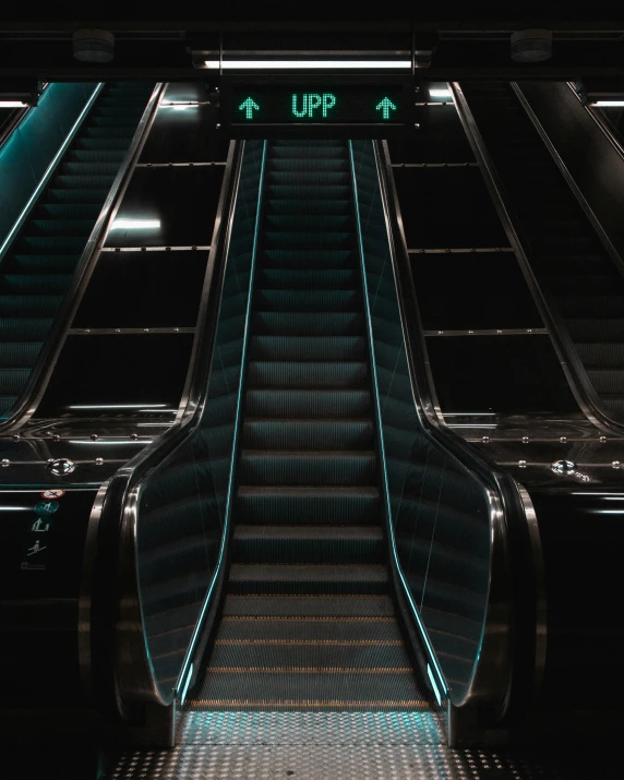 an escalator with light and electronic sign in a dark setting