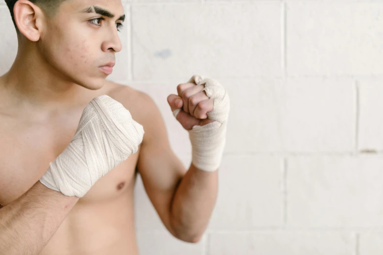 a shirtless man wearing white bandages and a t - shirt holds his fists