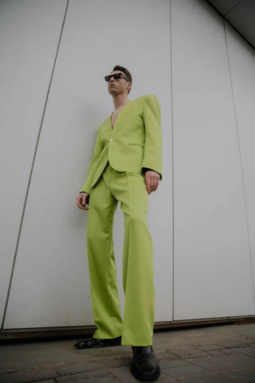 a man wearing sunglasses and suit posing by a wall