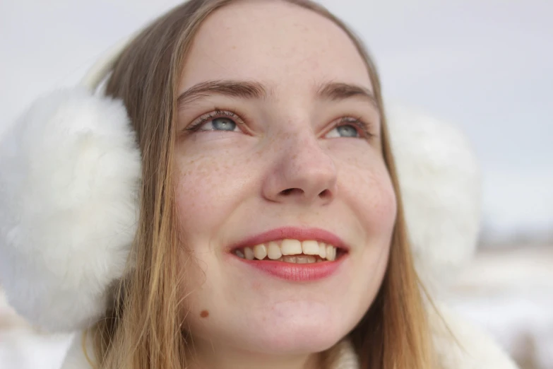 a woman wearing white ear muffs and looking up