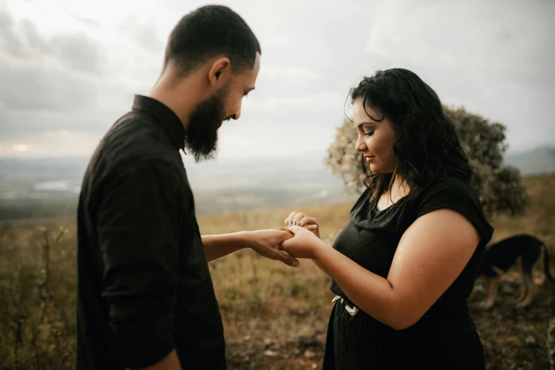 a pregnant man is holding his hand out for the woman to put a wedding ring on