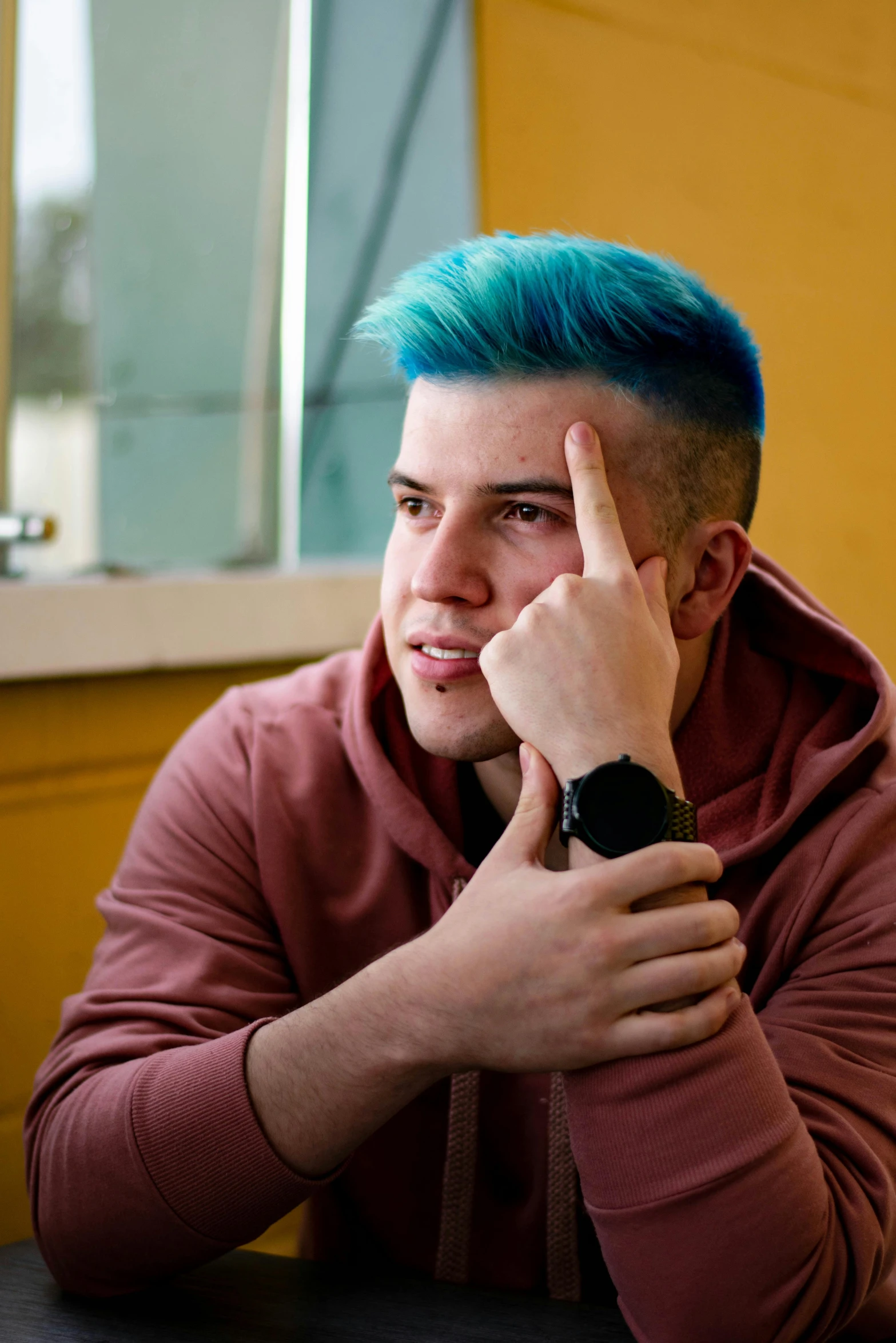 guy with blue hair sitting at table pointing finger toward his face