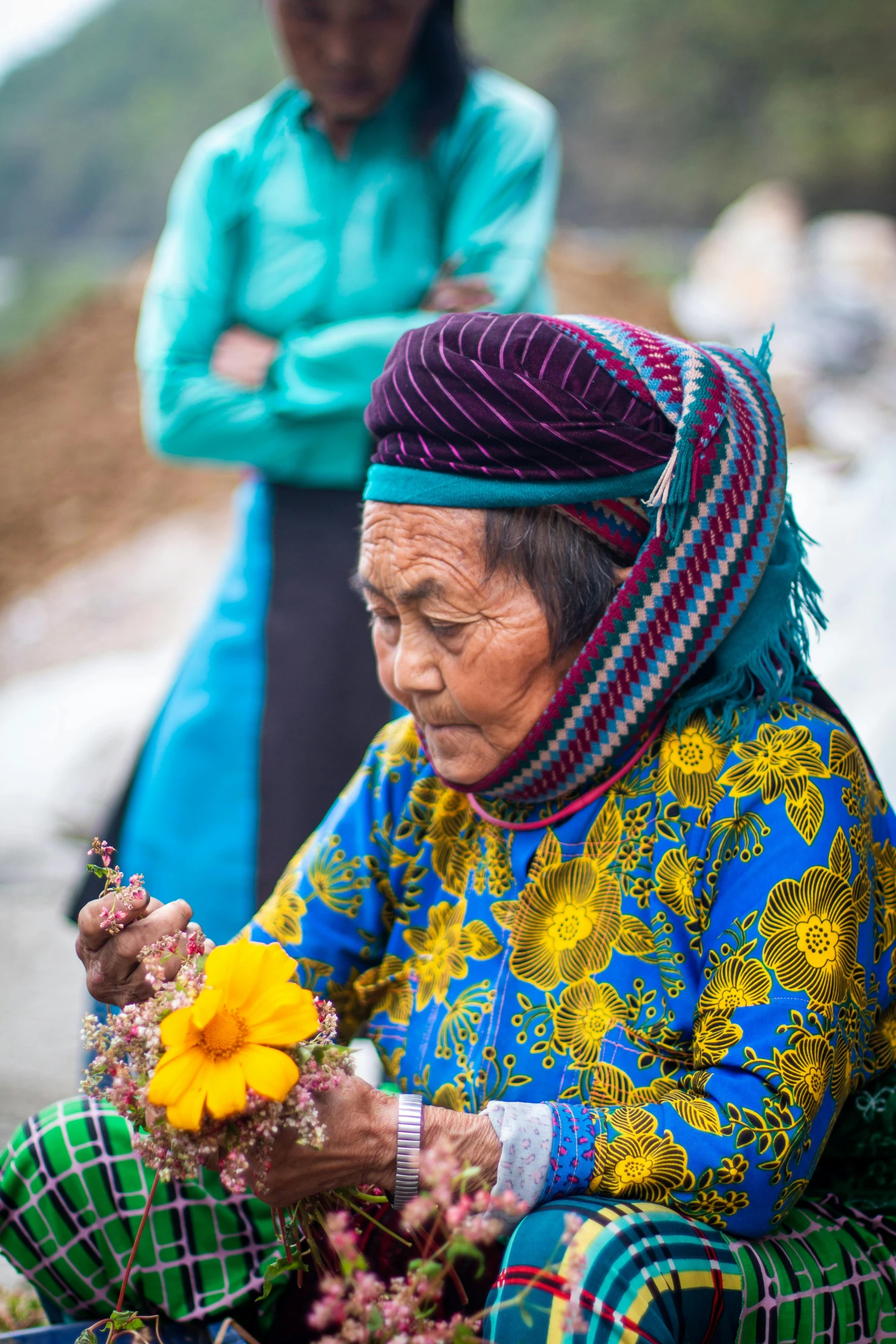 a woman sitting on the ground holding a yellow flower