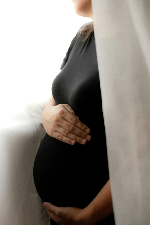 pregnant woman holding her belly under a curtain