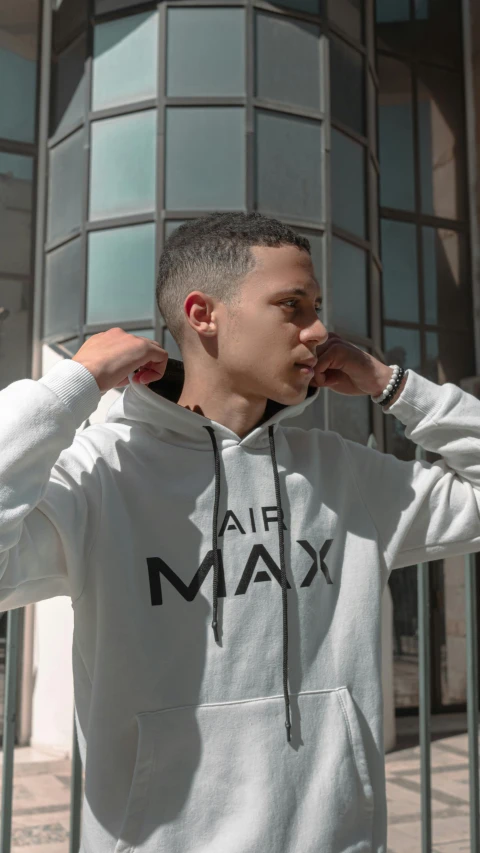 a young man in a white hoodie stands against a building