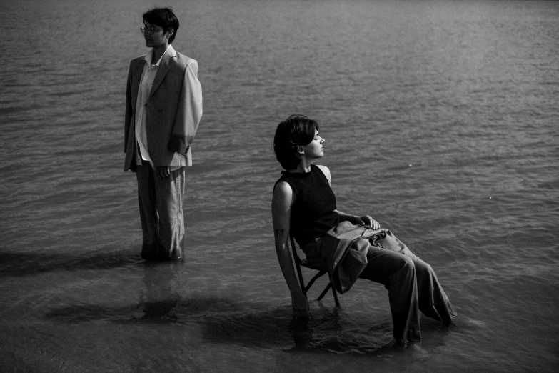 a young man sitting in a chair while another looks at him from the water