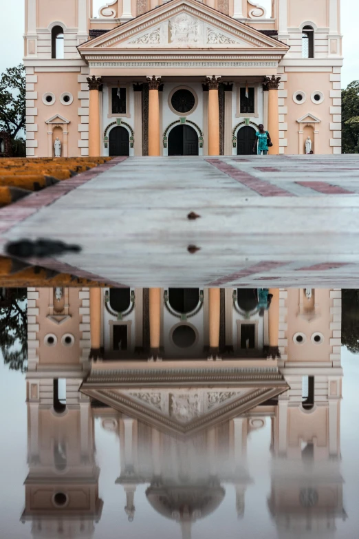 the white and beige building is reflected in the still water