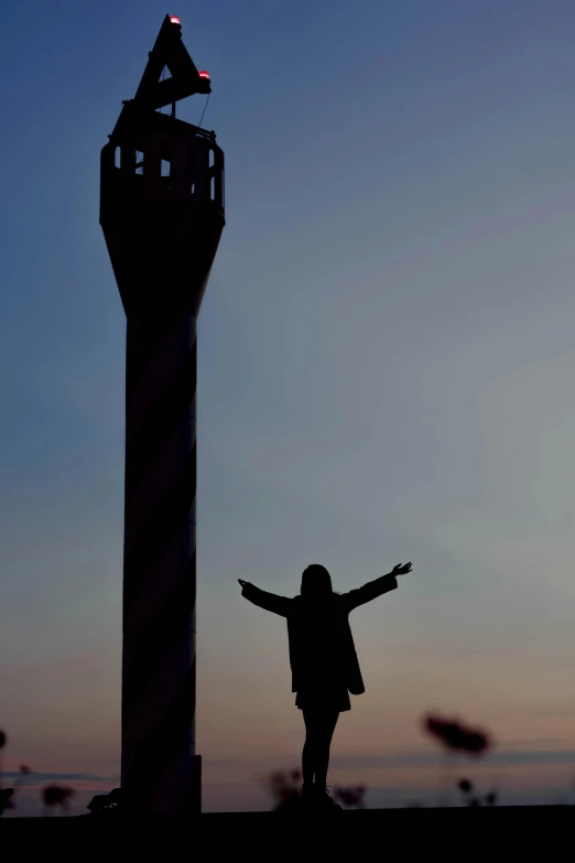 a silhouette of a girl with her arms outstretched standing in front of a tower