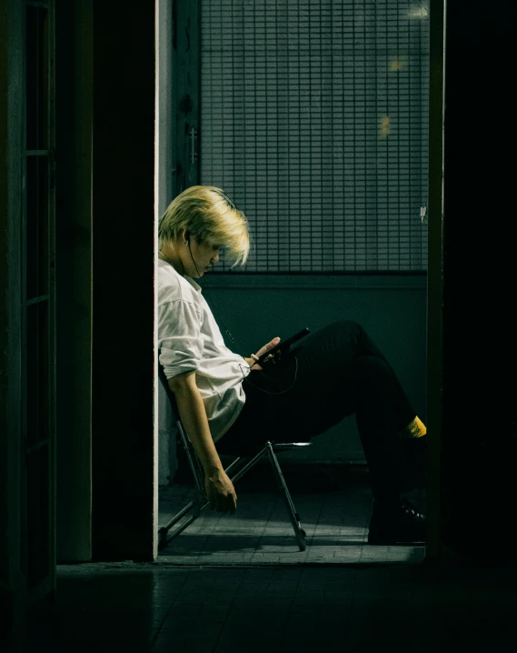 man sits in chair and looks down with back turned, dark background