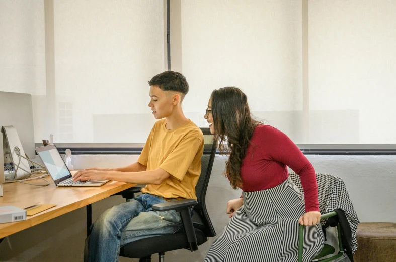 a woman is watching a man at a computer