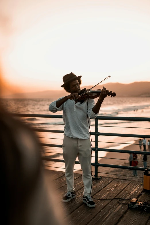 man with fiddle playing music on pier on sunset