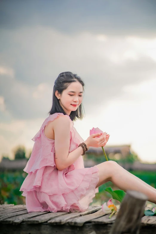 a beautiful young asian woman wearing a pink dress sits on a wooden platform