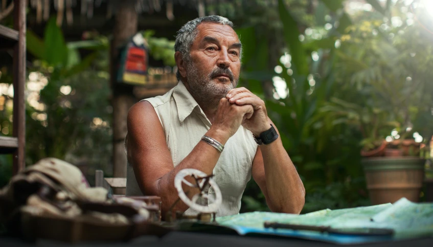 an older man sitting in front of a table full of other items