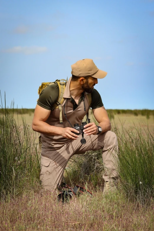 a man in brown work clothes and hat kneeling on field