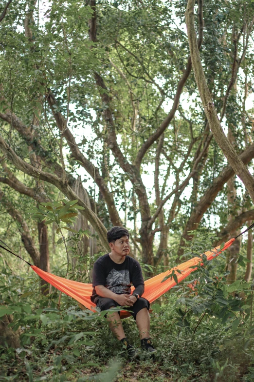 a man sitting on top of an orange hammock in a forest