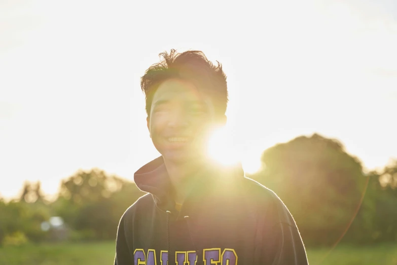 the sun shining through the tree and behind a smiling male in a hooded coat