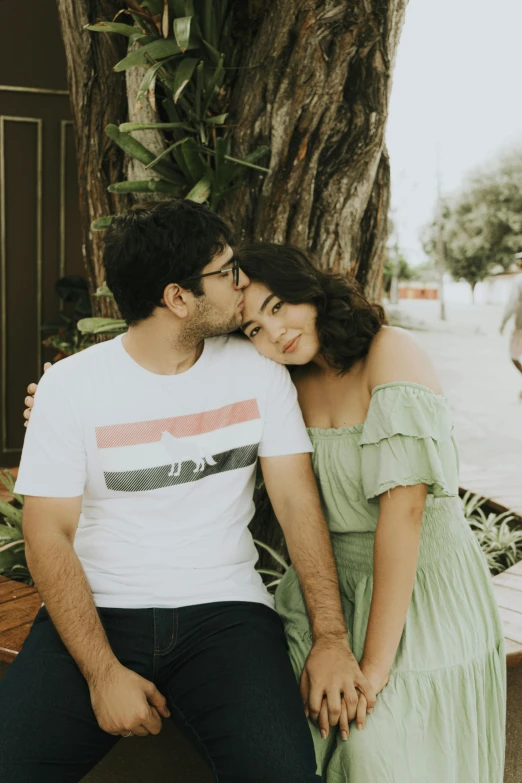 the couple is sitting on a bench in front of a tree