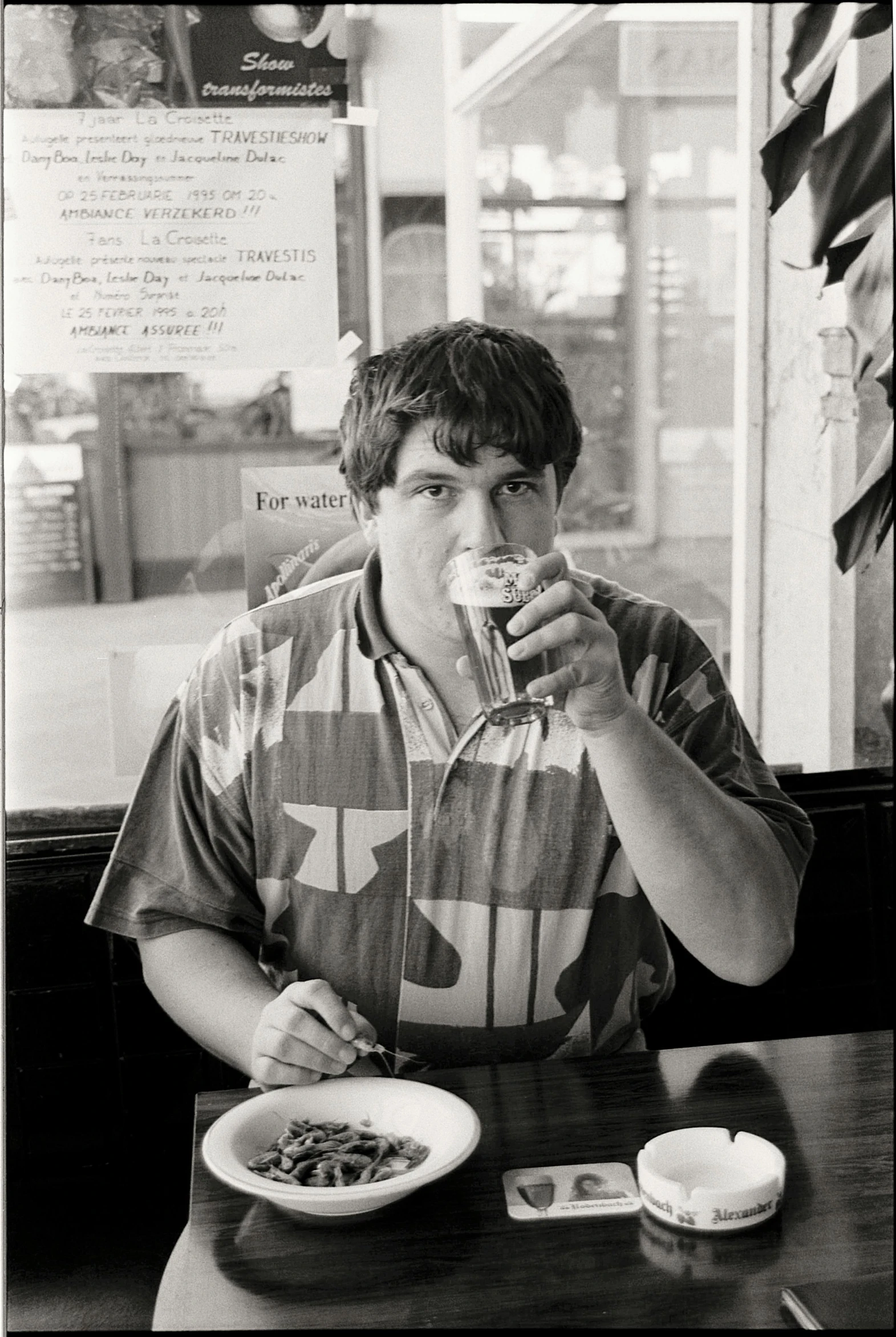 a young man drinking and eating noodles in front of the window