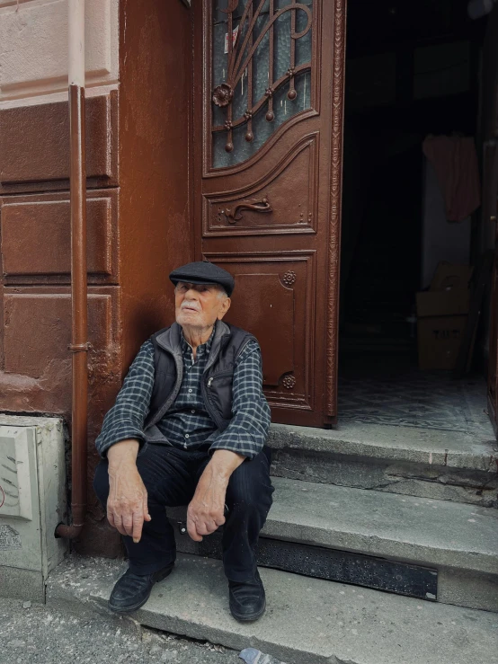 man with hat and vest sitting at front of a door