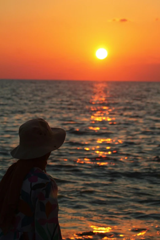 a person sitting on top of a beach with the sun setting