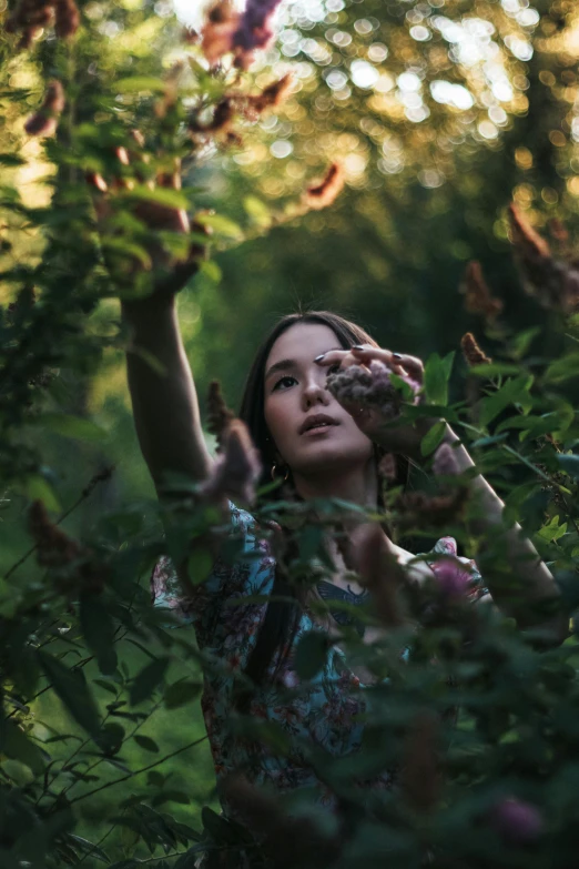 the woman is holding her hand up above her head while standing in the woods