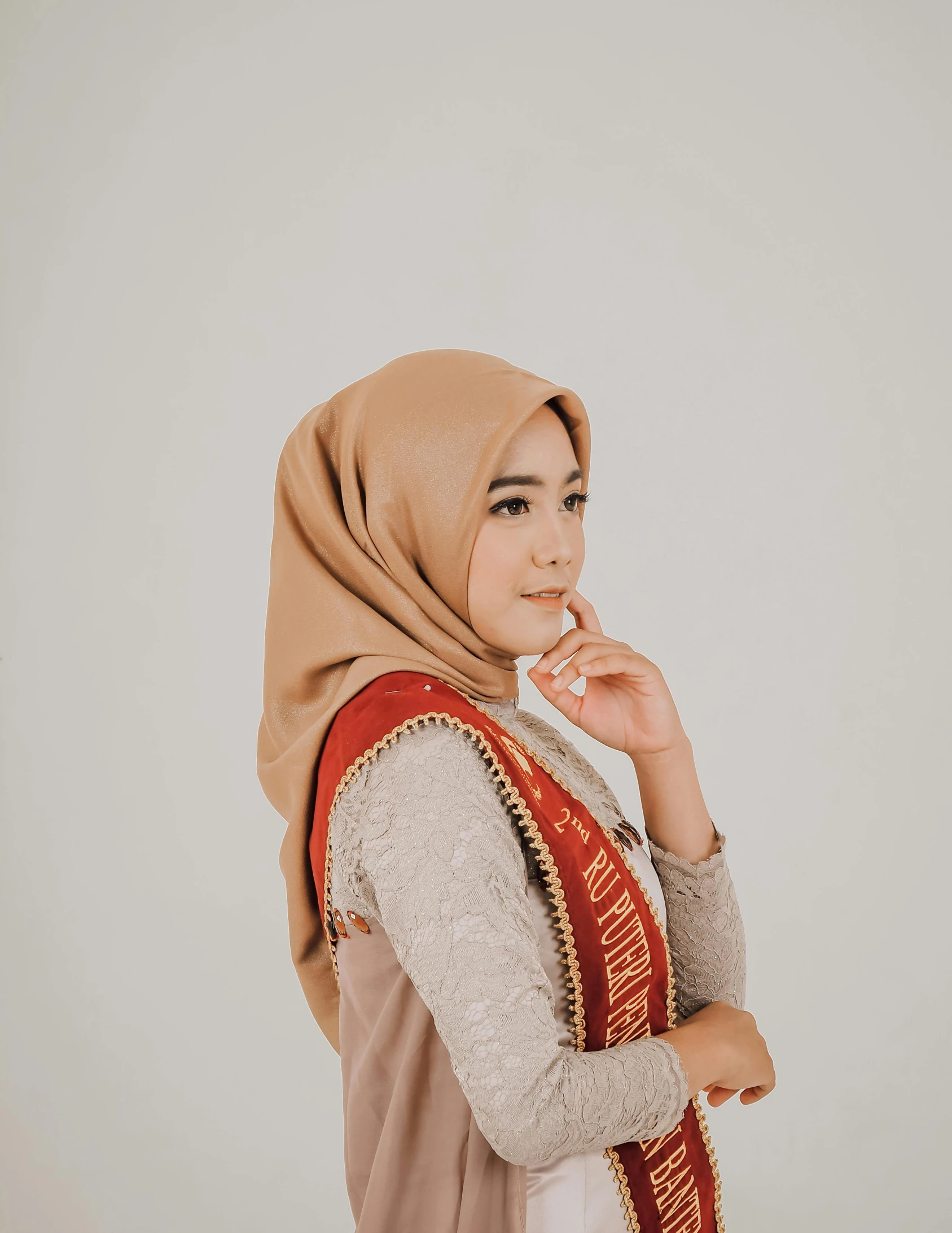 woman with brown headscarf and red shawl standing with hand on mouth