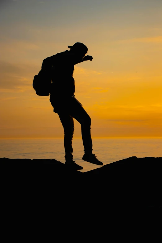 a man walking on a beach at sunset with a backpack