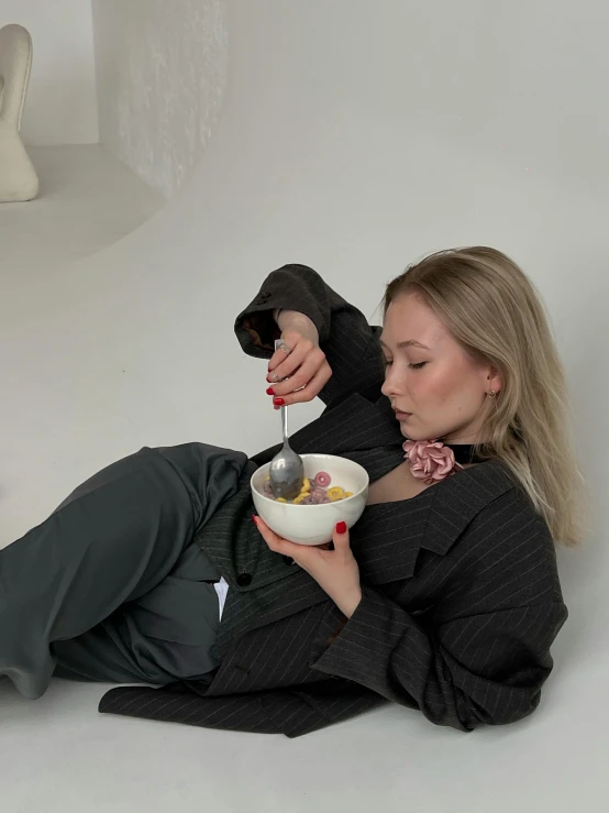a blonde woman eating cereal while sitting on the floor