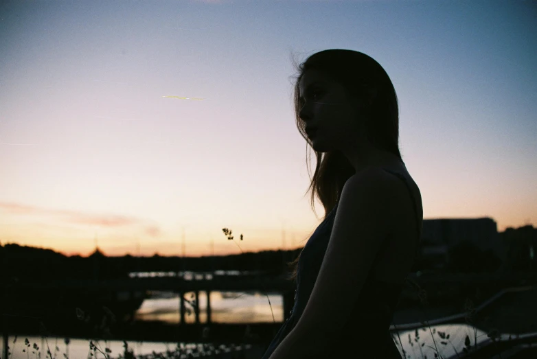 a woman in silhouette standing next to the water at sunset