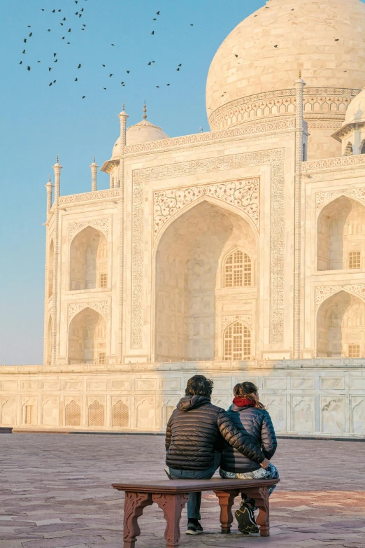 two people sitting on a bench looking at birds flying in the sky