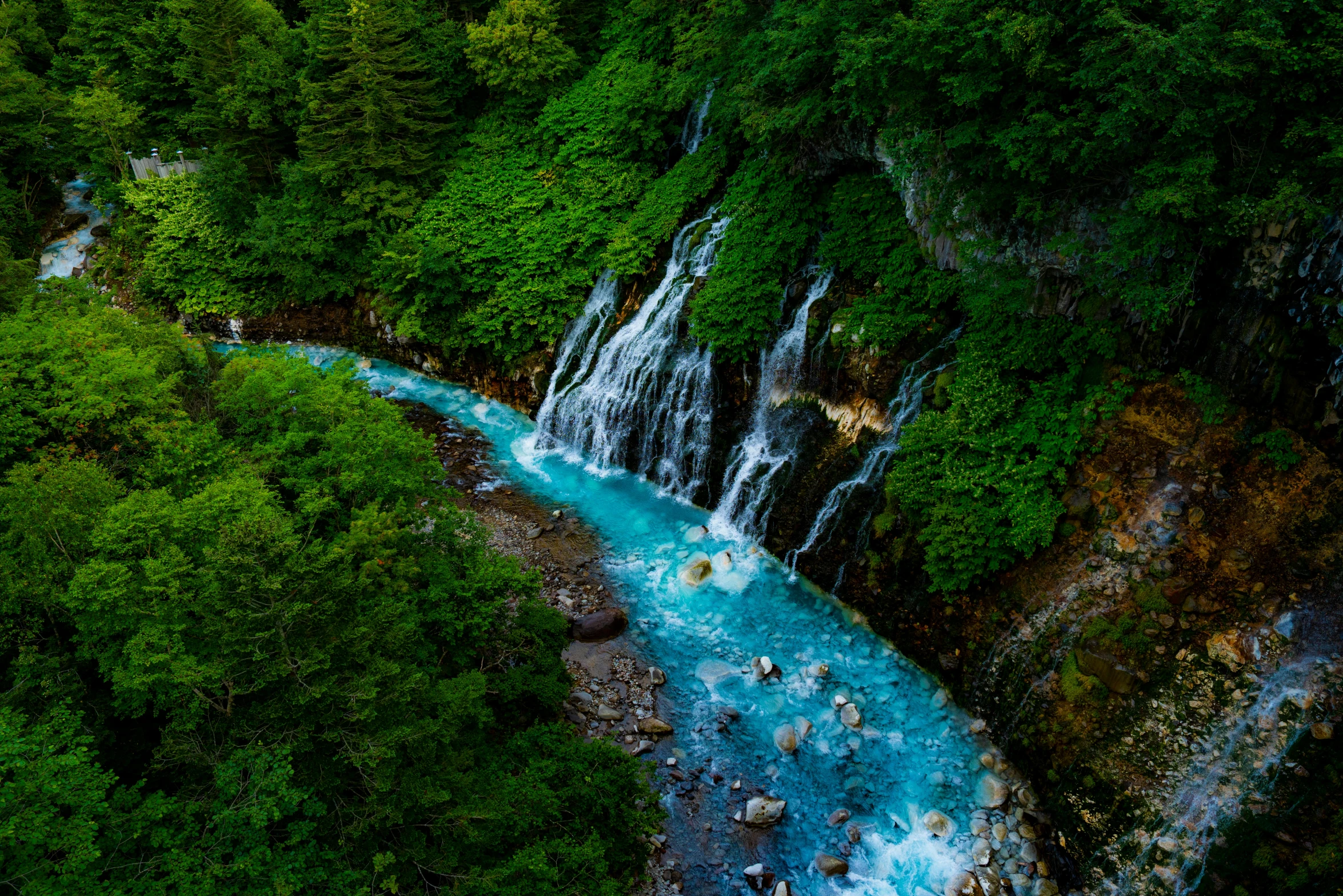 blue river running down a hillside surrounded by trees