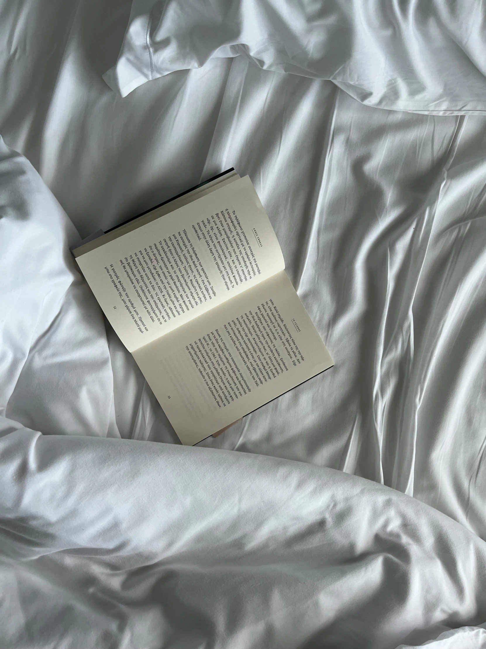 a book laying on top of an unmade bed with white sheets