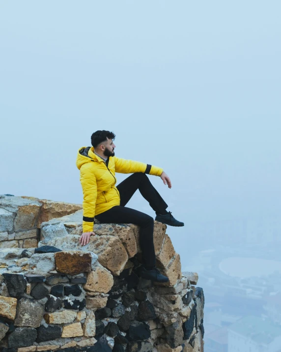 a man sitting on top of a rocky outcropping with a yellow jacket on