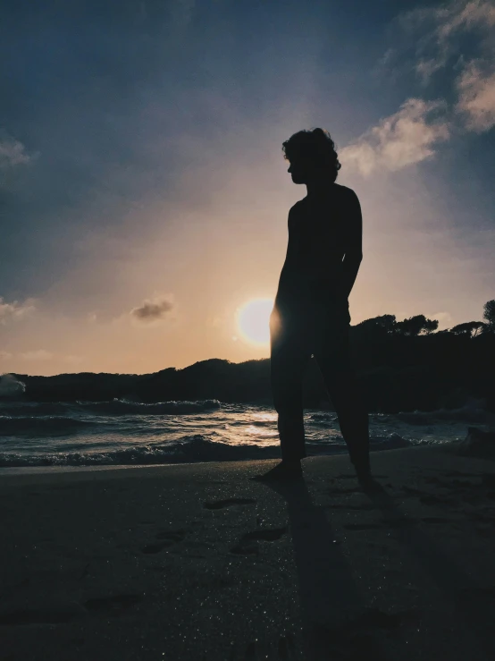 a man stands on the beach in the foreground at sunset