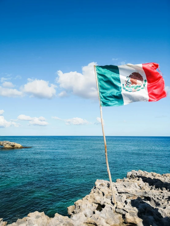 the flag of mexico is on a rocky shore