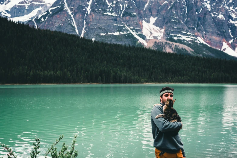 the man is standing near a mountain lake