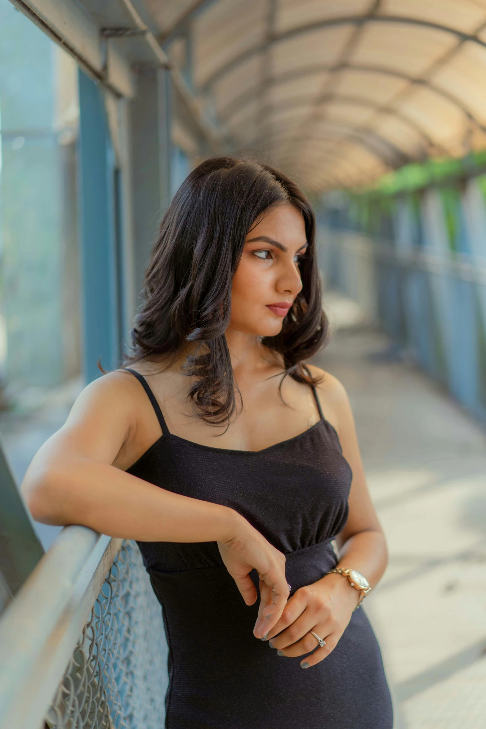 a woman in a black dress leaning on a metal fence