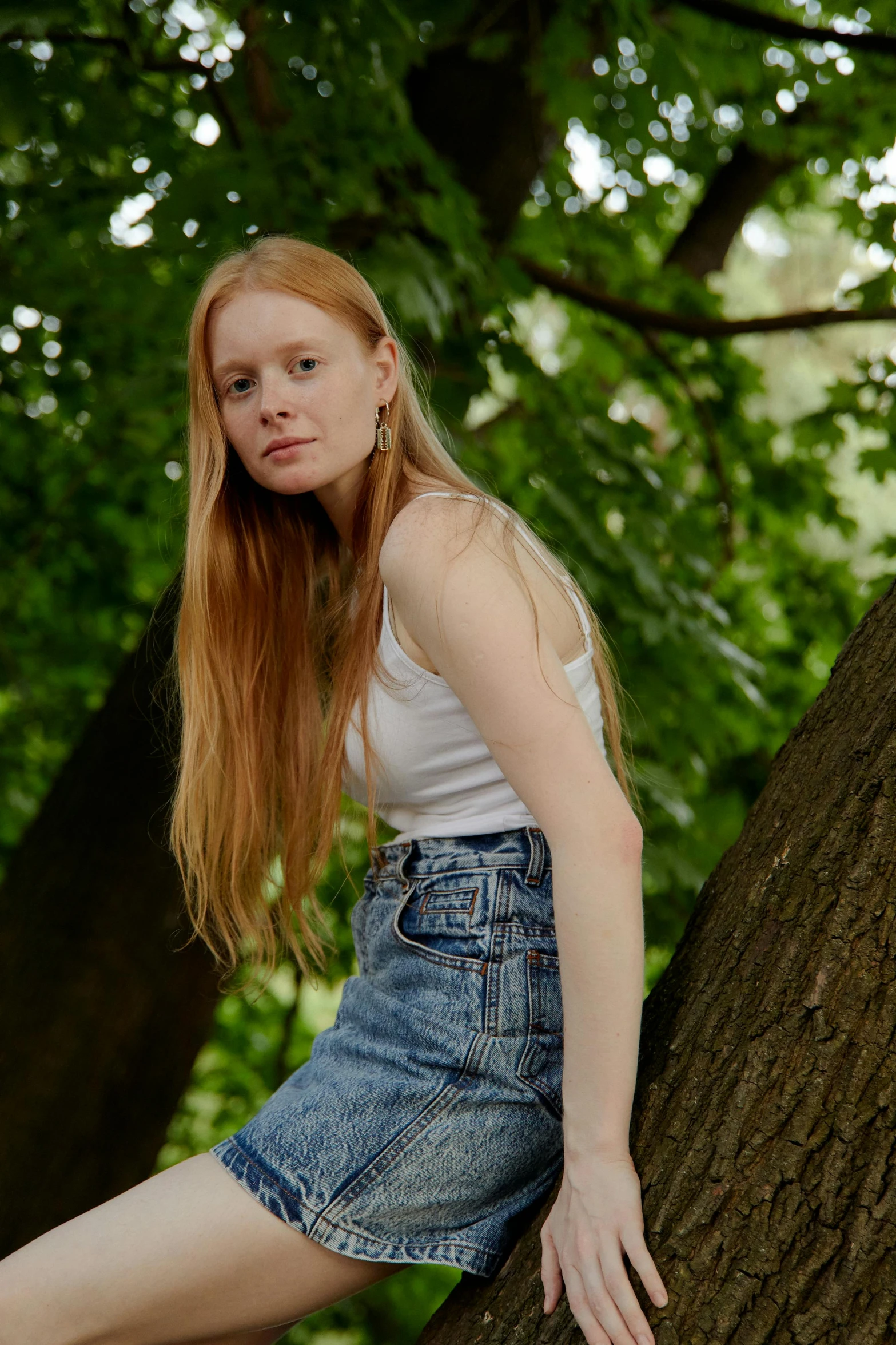 a young lady wearing denim skirts and top leaning on a tree trunk