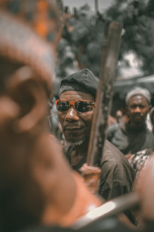 man in a crowd with large sculptural face and wooden objects