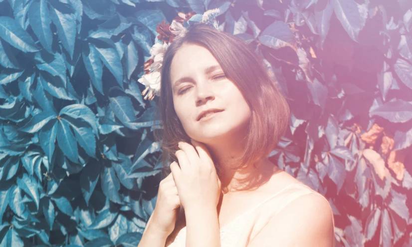 a woman wearing a floral crown standing in front of leaves