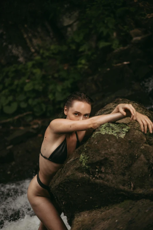 a woman with  is leaning on rocks near water