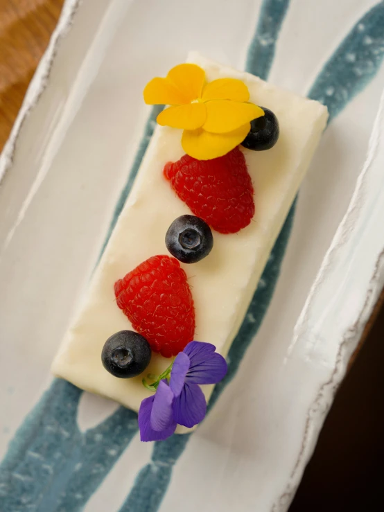 cake covered in white and cream has fruit and flowers on it