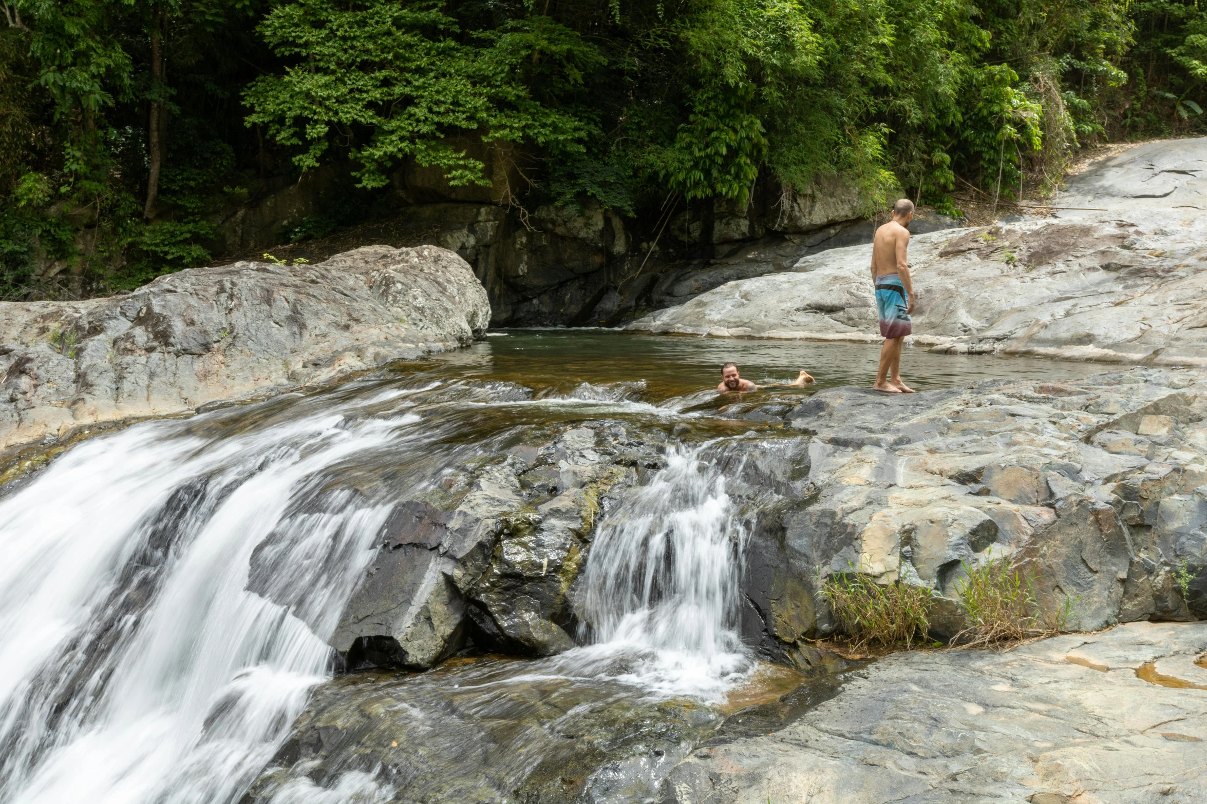 a boy standing on a large rock next to water