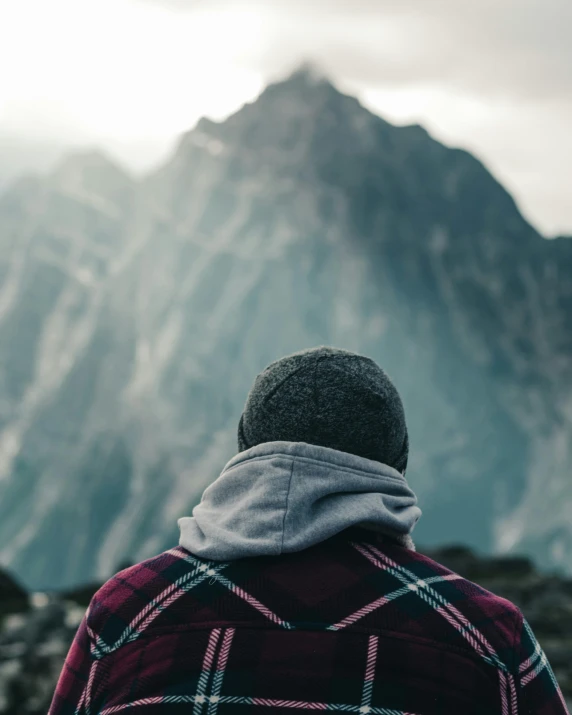 a man in plaid and black hat is looking out at mountains