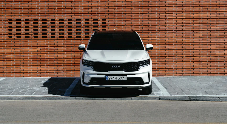 the front of a white suv parked by a brick wall