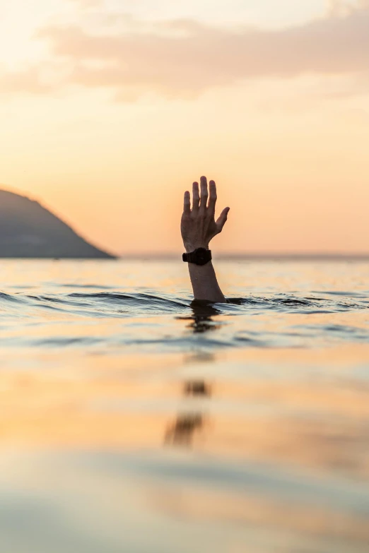 there is a hand in the water with a sunset behind it