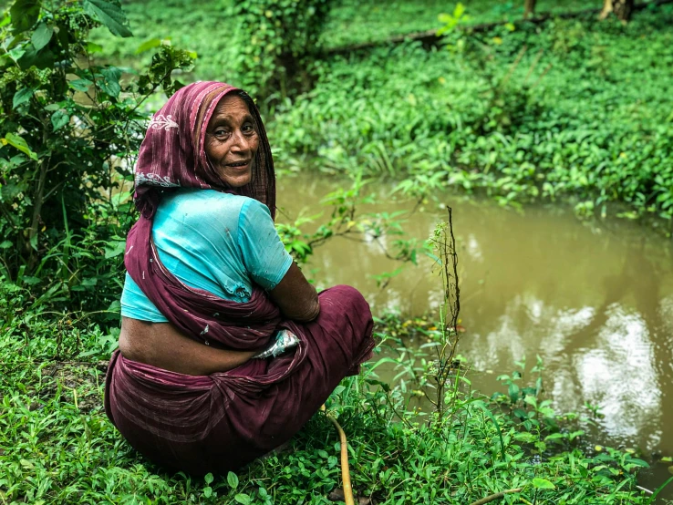 woman squatting in grass near water on a sunny day