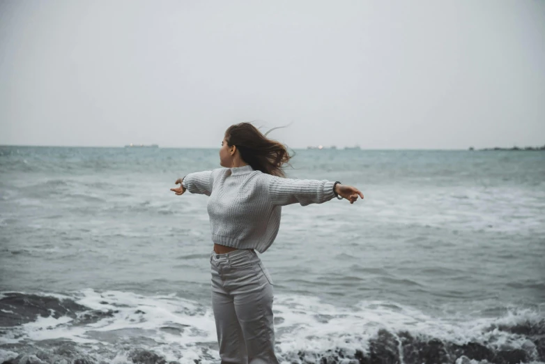 a woman in a sweater standing on the beach