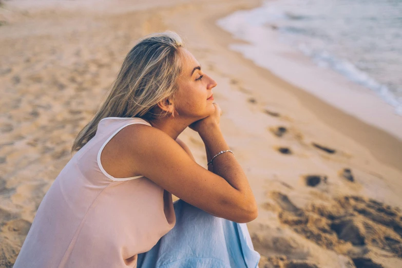 a woman in pink shirt sitting on the beach with her arm around her neck