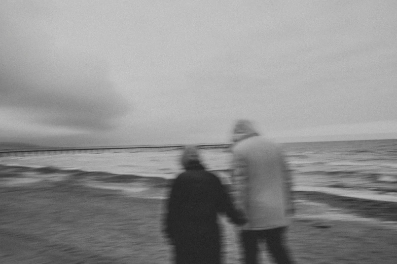 two men standing on a beach looking at the ocean